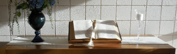 open bible on a table between a vase of flowers and candle in glass holder