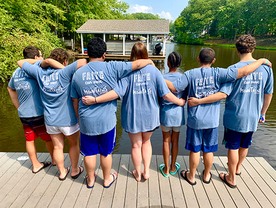 group of youth with backs to camera standing on a pier in matching t-shirts
